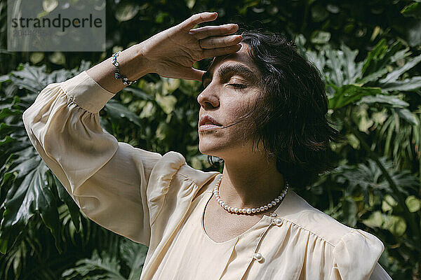 Woman with eyes closed touching forehead in front of plants