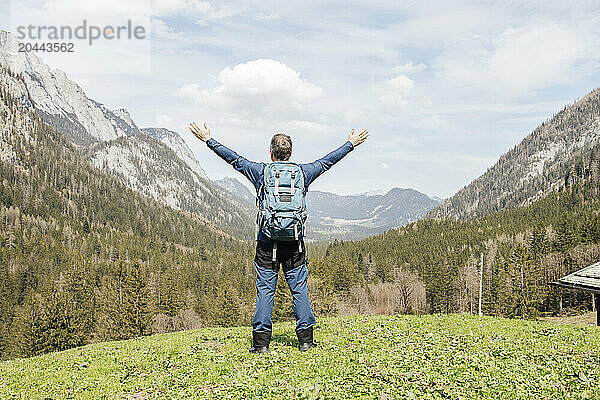 Carefree man standing with arms raised in front of mountains