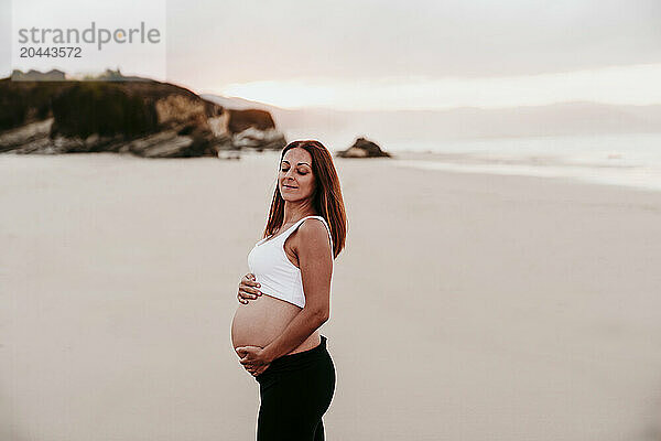 Smiling pregnant woman with eyes closed standing at beach