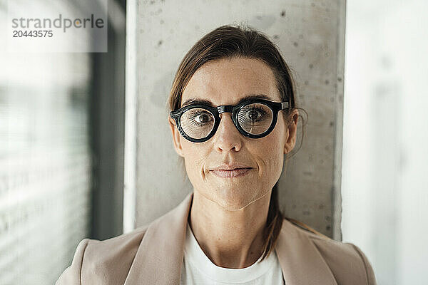 Businesswoman with eyeglasses leaning on wall at office