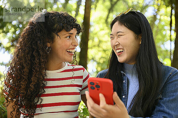 Cheerful friends holding smartphone and laughing together