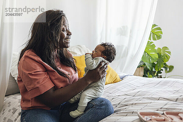 Mother playing with daughter and sitting on bed at home