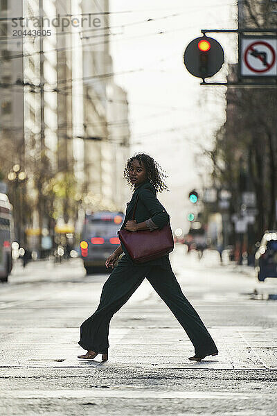 Young businesswoman with purse crossing road in city