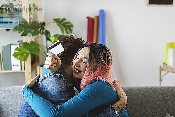 Happy woman holding credit card and hugging friend at home