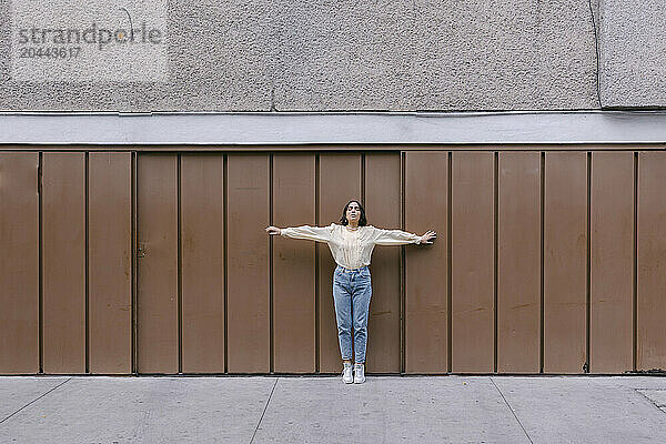 Woman standing with arms outstretched in front of brown wall