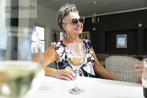 Happy woman sitting with wineglasses at table in resort