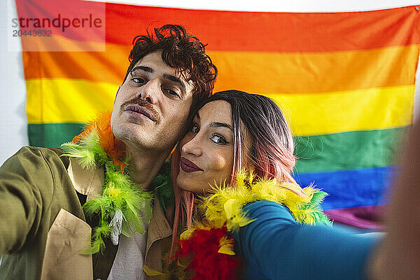 Happy non-binary people taking selfie in front of rainbow flag