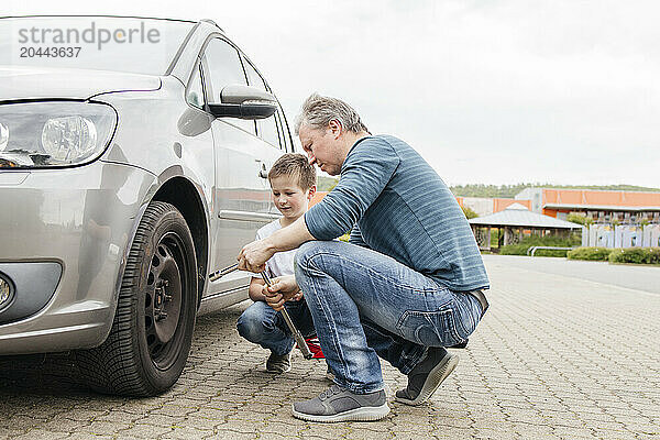 Father teaching about wrench to son by car