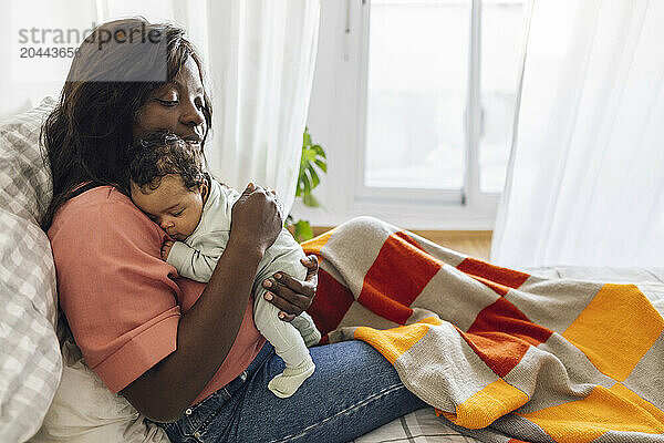 Mother embracing daughter and sitting on bed at home