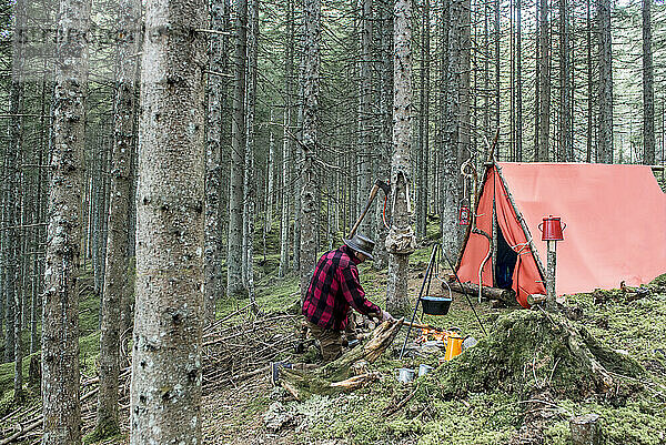 Senior man preparing bonfire near tent in forest