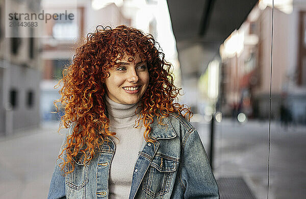 Smiling beautiful redhead young woman with curly hair wearing denim jacket