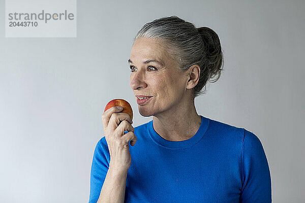 Senior woman holding apple in front of wall