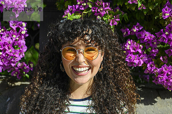 Smiling woman with yellow sunglasses standing near flowers