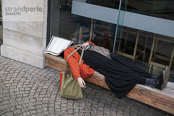 Tired young woman with newspaper lying on bench