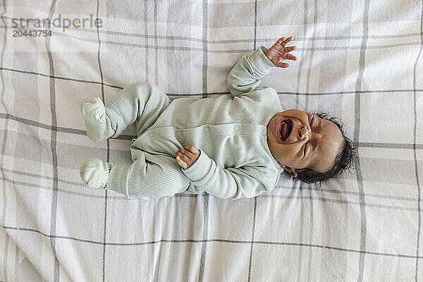 Crying baby girl lying down on bed at home