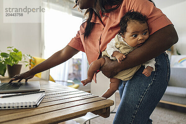 Freelancer carrying daughter and working on laptop at home