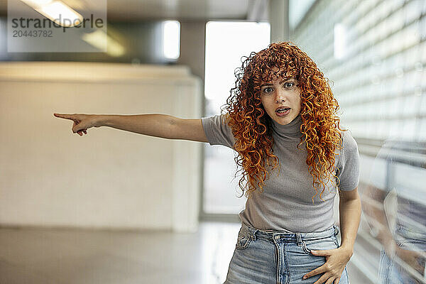 Angry redhead young woman with curly hair pointing away