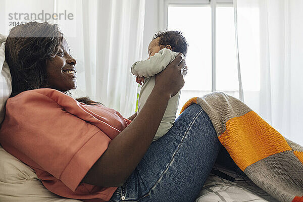 Happy mother playing with daughter and sitting on bed at home