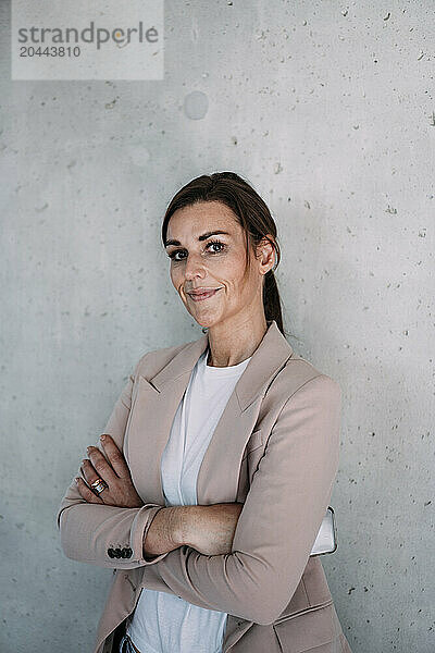 Businesswoman with arms crossed leaning at wall