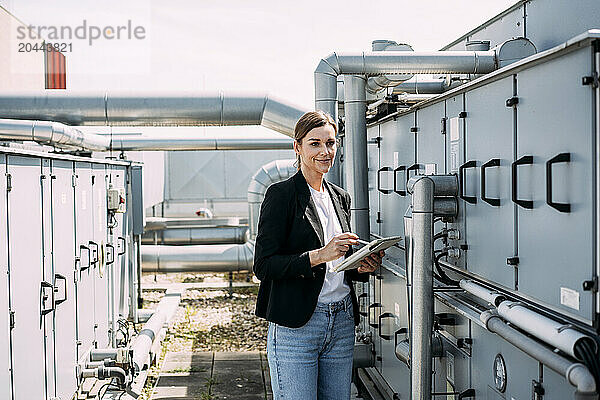 Businesswoman using tablet PC and examining factory machine