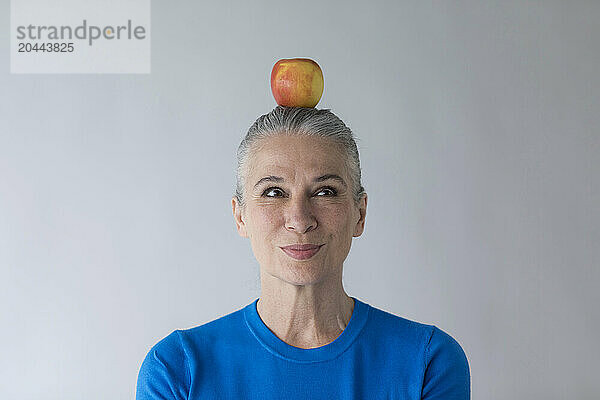 Smiling senior woman balancing apple on head