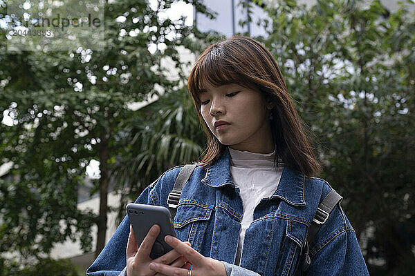 Woman using smart phone in front of trees