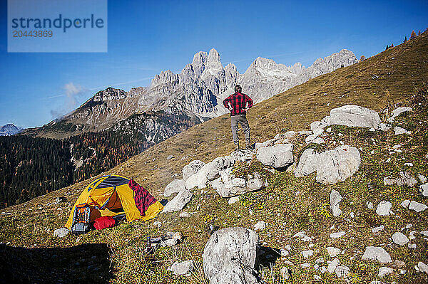 Senior man standing with hands on hip near tent and looking at mountain