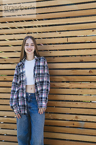 Happy girl standing in front of wooden wall