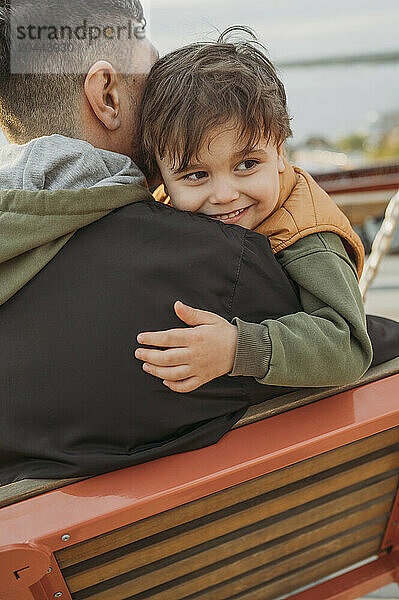 Smiling boy leaning on father's shoulder at park