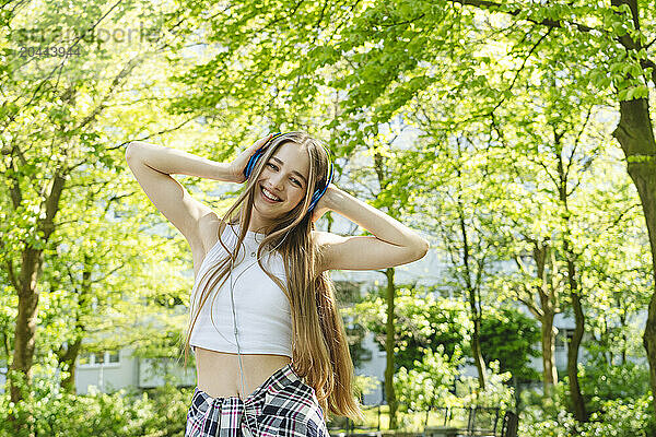 Happy teenage girl listening to music through headphones near trees