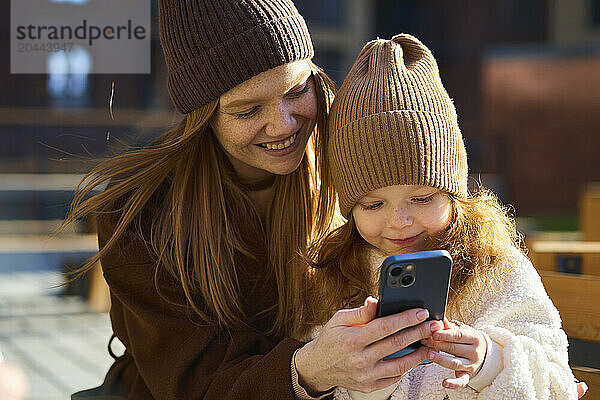 Happy woman using smart phone with daughter on sunny day