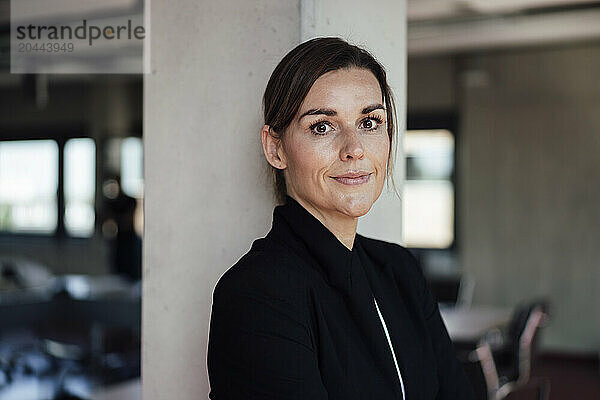 Smiling businesswoman wearing black blazer standing at office