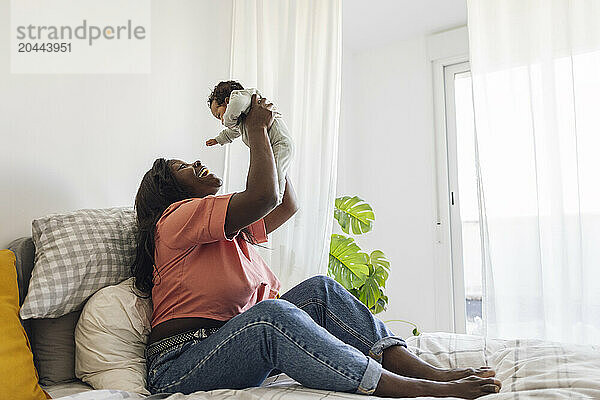 Playful mother lifting daughter and sitting on bed at home