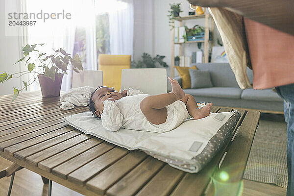 Baby girl lying down on wooden table in living room at home