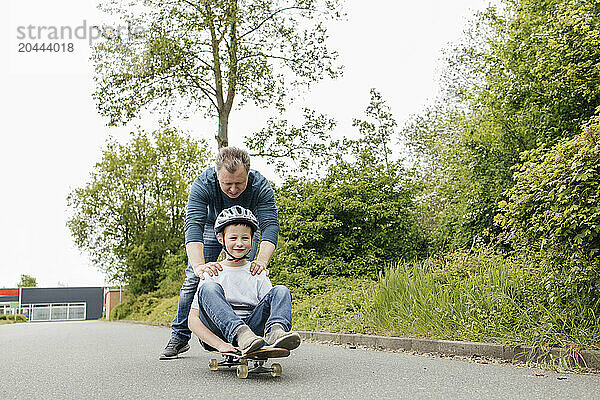 Father pushing son sitting on skateboard