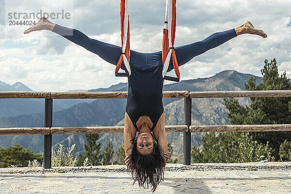 Woman with legs apart hanging upside down on silk practicing aerial yoga