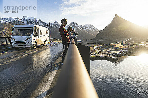 Norway  Nordland County  Group of young people standing on coastal bridge in Lofoten islands at sunset