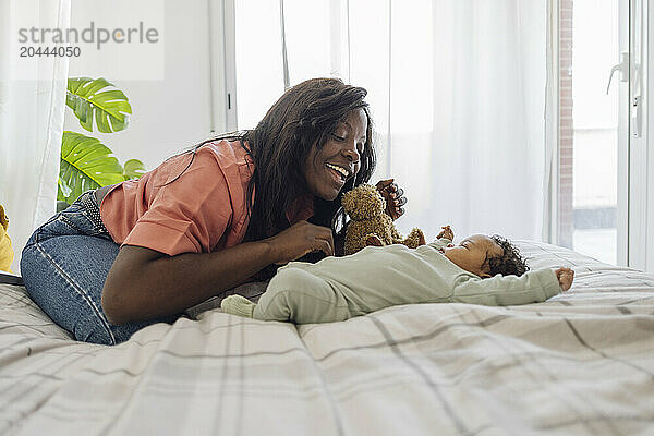 Mother playing with daughter lying down on bed at home