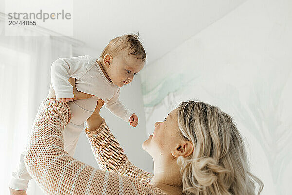 Blond woman lifting son at home