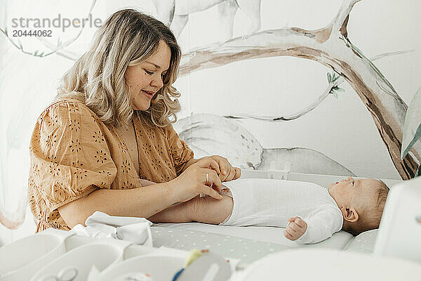 Blond mother changing clothes of baby boy on table