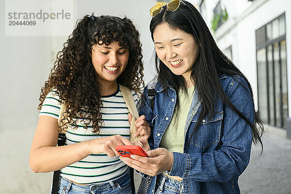 Smiling friends sharing smartphone at street