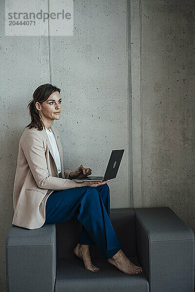 Thoughtful businesswoman sitting on armchair and using laptop at office