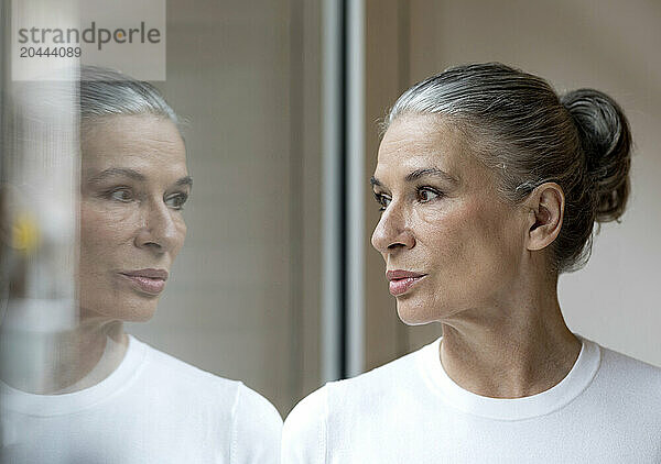 Retired gray haired woman looking out through window