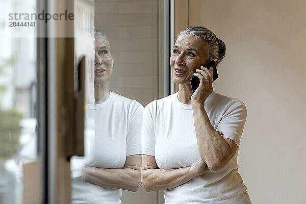 Senior woman talking on mobile phone looking out through window