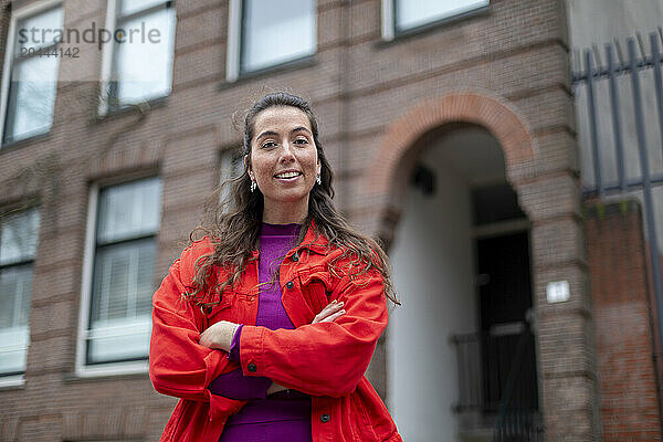 Smiling woman with arms crossed standing in front of building