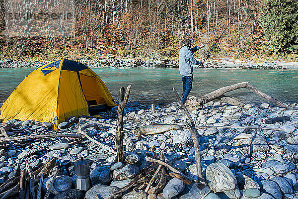 Senior man fishing with rod in river near tent on sunny day