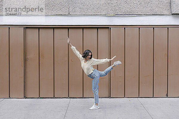 Cheerful woman dancing and having fun in front of brown wall