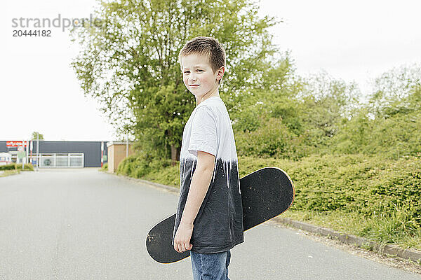 Boy with skateboard standing on road