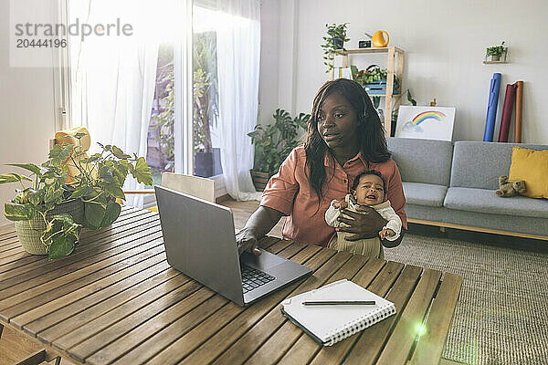 Focused working mother multi-tasking sitting near table at home office