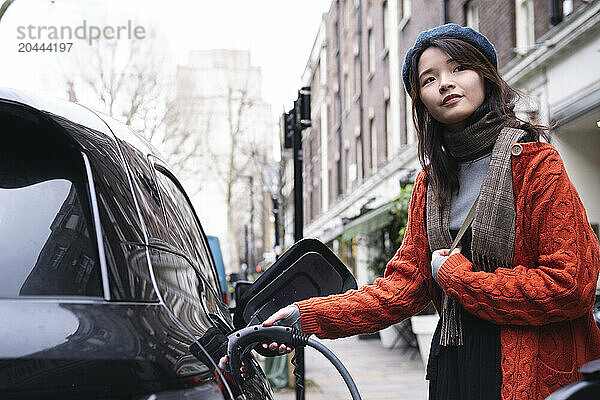 Young woman charging electric car at station